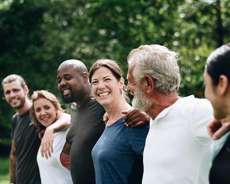Six people outdoors touching shoulders are smiling
