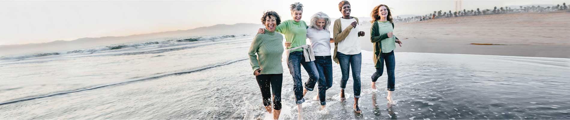 Five women laughing and kicking the water on the beach